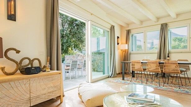 A modern living room with a glass table, wicker chairs, a sofa, and a dining area with a table and chairs. - Appartamento Mare di Spartaia (Marciana)