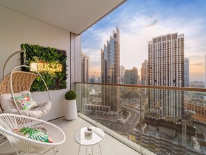 A balcony with a hanging chair, a small table, and a neon sign for SKY Apartments.
