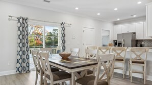 Une cuisine moderne avec des meubles blancs, un réfrigérateur en acier inoxydable et un coin repas comprenant une table et des chaises en bois.