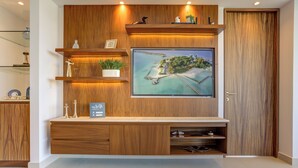 A modern living room with a large flat-screen TV mounted on a wooden wall, surrounded by shelves and a cabinet. - Altamar Canal View Condos (Nuevo Nayarit)