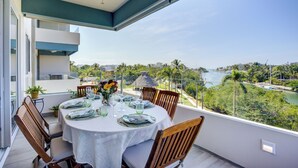 A dining area with a table set for four, overlooking a scenic view of a river and greenery. - Altamar Canal View Condos (Nuevo Nayarit)