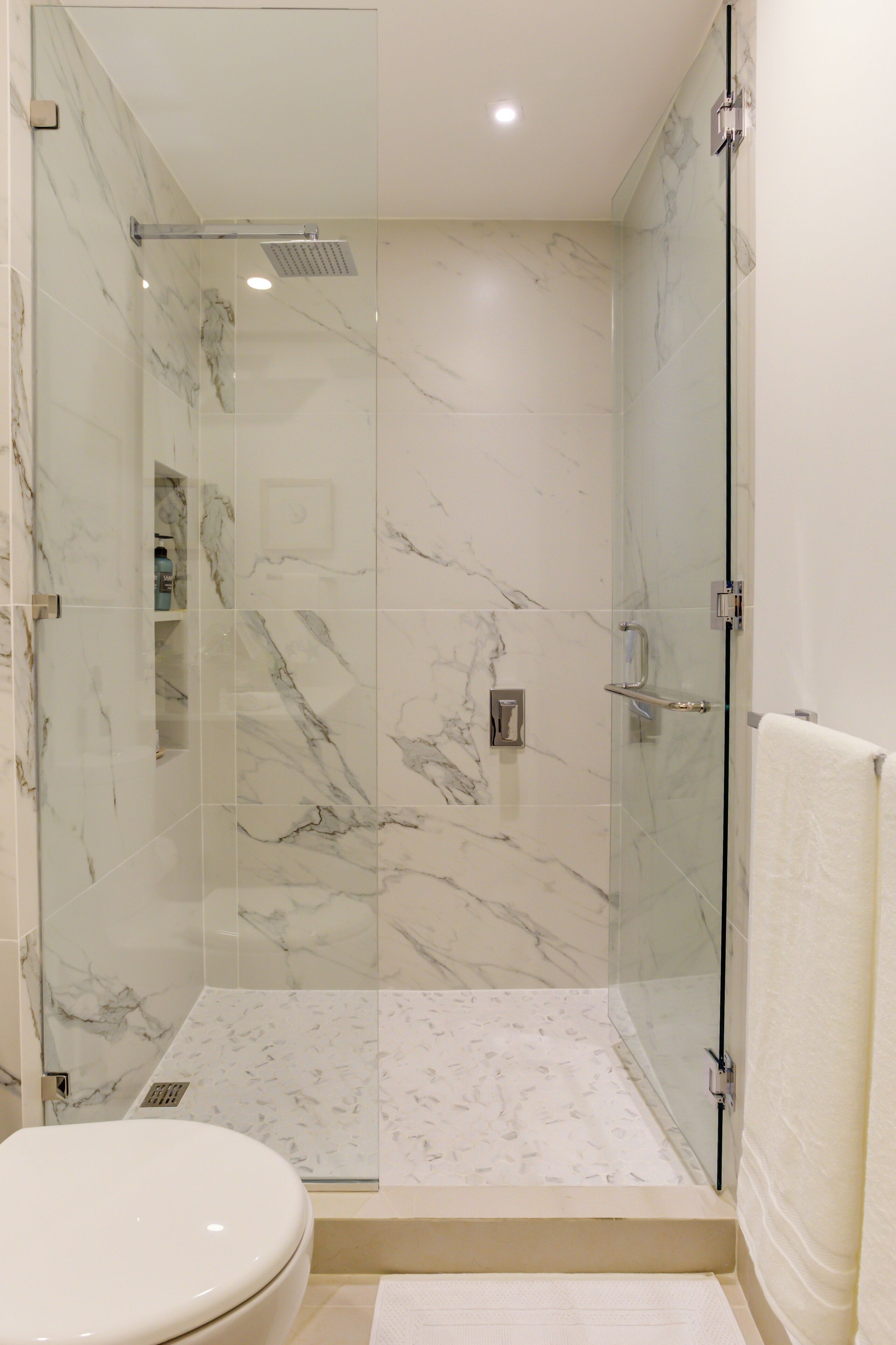 A modern bathroom with a glass-enclosed shower, marble tiles, and a white toilet.