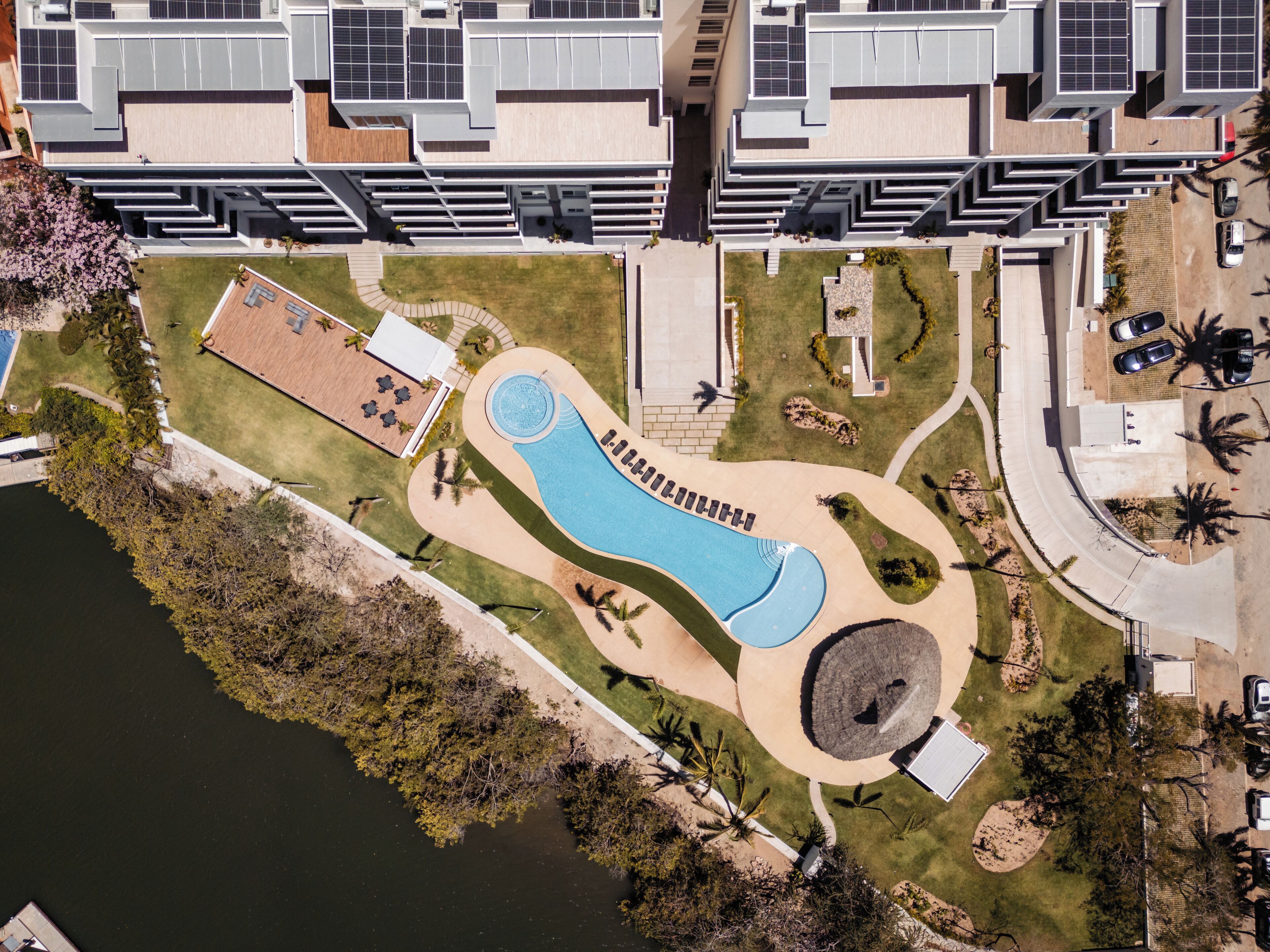 Vue aérienne d’un complexe résidentiel moderne doté d’une piscine, de jardins aménagés et de panneaux solaires installés sur les bâtiments.