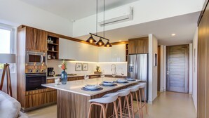 A modern kitchen with a central island, built-in appliances, and bar stools. - Altamar Canal View Condos (Nuevo Nayarit)