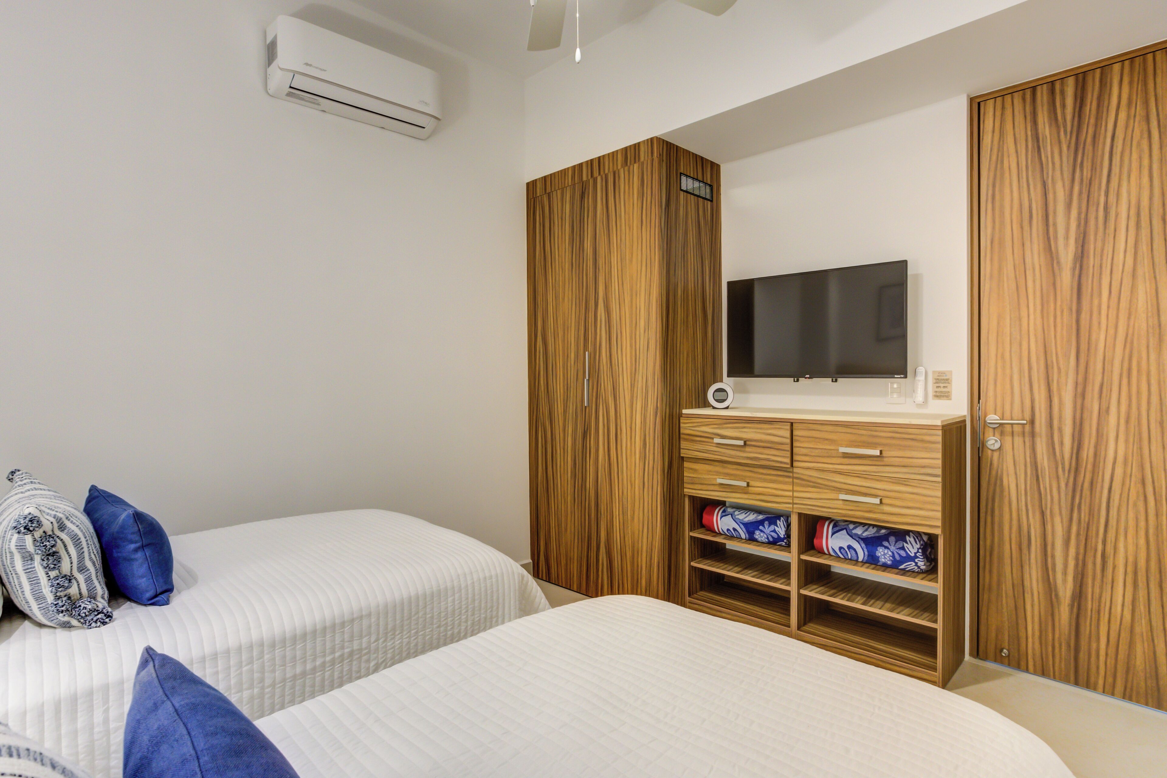 Un dormitorio con dos camas, un armario de madera, un televisor de pantalla plana y un estante empotrado con toallas.