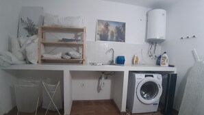 A compact kitchen with a washing machine, a sink, and a shelf with folded towels. - Charming 2BR/2BA apartment with pool - 32 nights minimum! (El Pilar de la Mola)