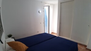 A bedroom with a bed, a nightstand, a potted plant, and a door leading to a balcony. - Charming 2BR/2BA apartment with pool - 32 nights minimum! (El Pilar de la Mola)