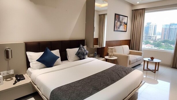 A modern hotel room with a large bed, bedside tables, a sofa, a small round table, and a large window with a city view. - Hotel Shri Sai Deluxe - 1 Min from Adarsh Nagar Metro | Couple, Business, and Family Friendly (New Delhi)