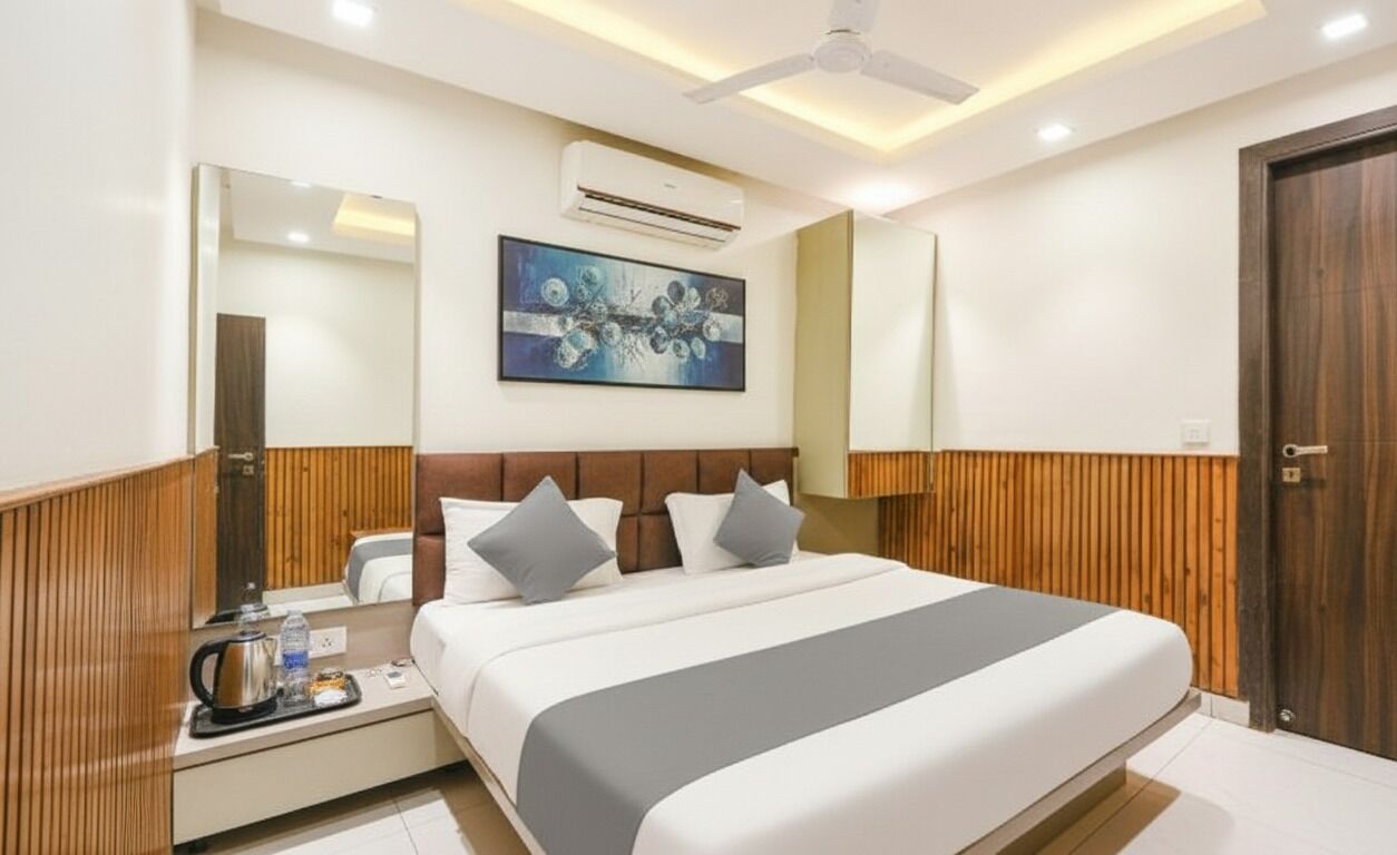 A modern hotel room with a large bed, wooden paneling, a ceiling fan, an air conditioning unit, a painting on the wall, and a wooden door.
