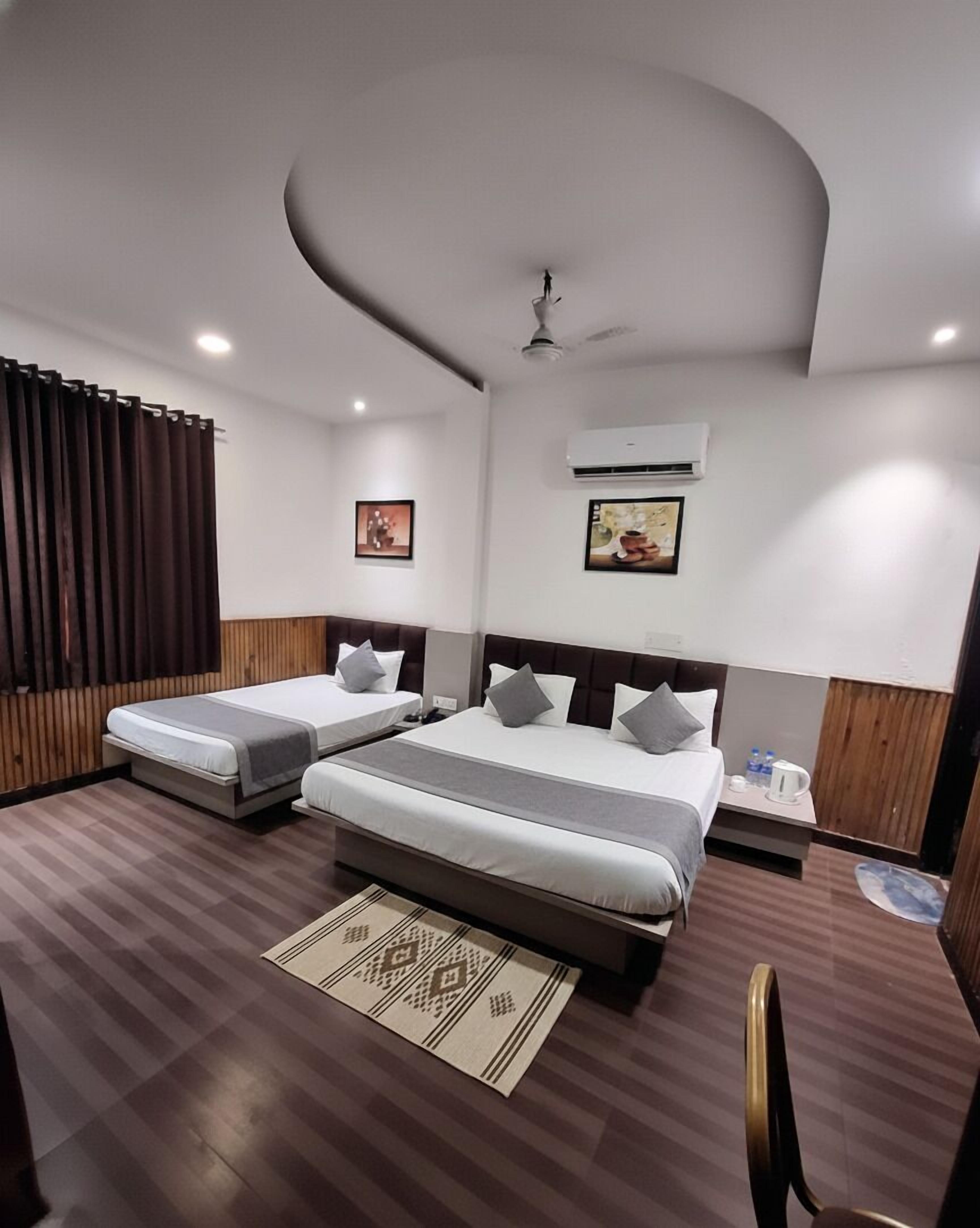 Une chambre d’hôtel avec deux lits, un ventilateur de plafond, un climatiseur et une petite table avec une bouilloire et des bouteilles d’eau.