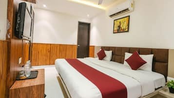 A hotel room with a bed, a wooden panel wall, a television, an air conditioning unit, and a small plant.