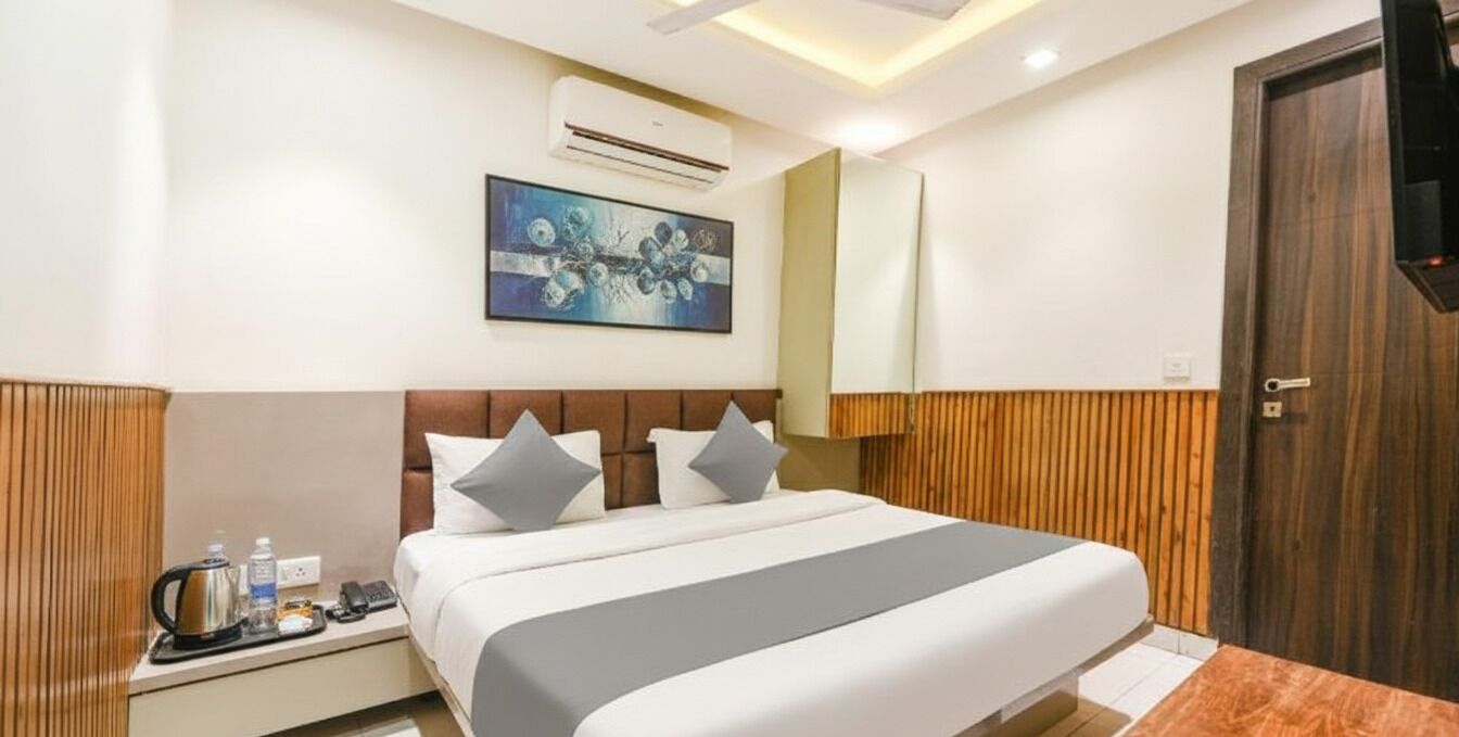 A hotel room with a bed, bedside table, and a painting on the wall.
