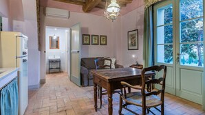 Un coin repas chaleureux avec une table et des chaises en bois, un luminaire suspendu et une vue sur l’extérieur par une porte verte.
