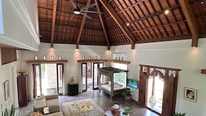 Un vaste espace intérieur doté d’un haut plafond, d’un grand coin salon avec des canapés et une table basse, et d’une vue sur l’extérieur grâce à une porte ouverte.