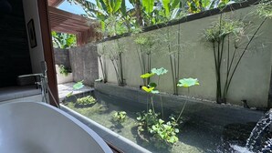Un espace spa comprenant un bain à remous, une petite fontaine et une végétation luxuriante, notamment des bananiers et de hautes herbes.