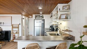 A modern kitchen with a central island, stainless steel appliances, and wooden ceiling accents. - 68th St Oceanfront Condo with Pool (Ocean City)