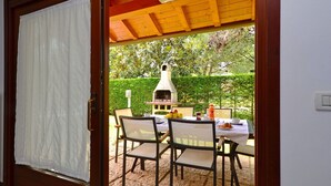 Een terras met een barbecue, stoelen en een eettafel.