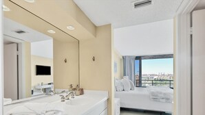 A modern hotel room with a large bed, a bathroom with a vanity, a flat-screen TV, and a view of the city.