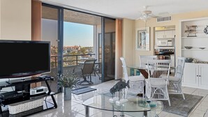 A modern living room with a flat-screen TV, glass coffee table, and white wicker chairs.