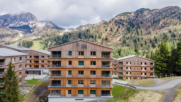 A multi-story wooden building with balconies, set against a mountainous backdrop. - Exclusive apartment right on the piste (Sonnenalpe Nassfeld)