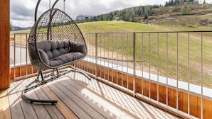 A wooden deck with a hanging chair and a view of a green landscape. - Exclusive apartment right on the piste (Sonnenalpe Nassfeld)