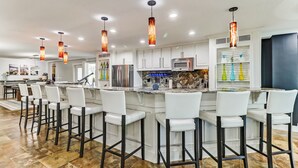 Una cocina moderna con armarios blancos, electrodomésticos de acero inoxidable y una isla central con taburetes de bar.