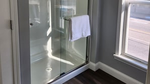 Une douche fermée par des parois de verre, avec une serviette blanche accrochée à la poignée de la porte.