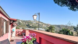 A balcony with a table, a potted plant, and a view of a hillside with houses. - La Quiete e il Mare by Interhome (Imperia)