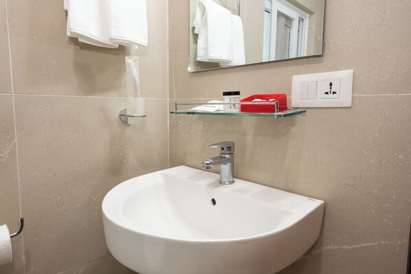 Un baño con lavamanos blanco, estante de vidrio, espejo y toallero.
