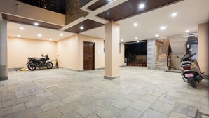 A spacious covered outdoor area with tiled flooring, a motorcycle, and a scooter parked. - Mandevilla Home (Lalitpur)