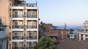 A multi-story residential building with balconies, air conditioning units, and a view of distant mountains. - Mandevilla Home (Lalitpur)