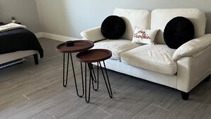 A modern living room with a white sofa, two black round tables, and a bed with a dark headboard.