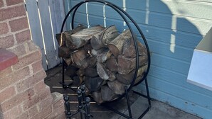 A stack of firewood in a metal rack against a blue door.