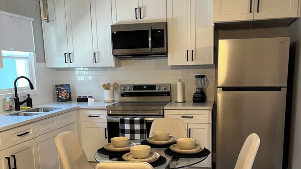 A modern kitchen with white cabinets, stainless steel appliances, and a dining area with beige chairs.