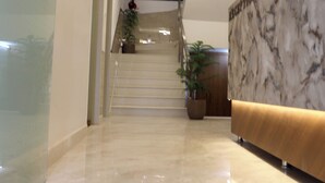 Un vestíbulo moderno con una recepción de mármol, un ventilador de techo y una escalera que conduce a un piso superior.