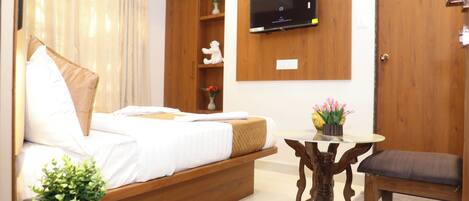 A hotel room with a bed, bedside table, TV mounted on the wall, a wooden door, and a small table with a chair.