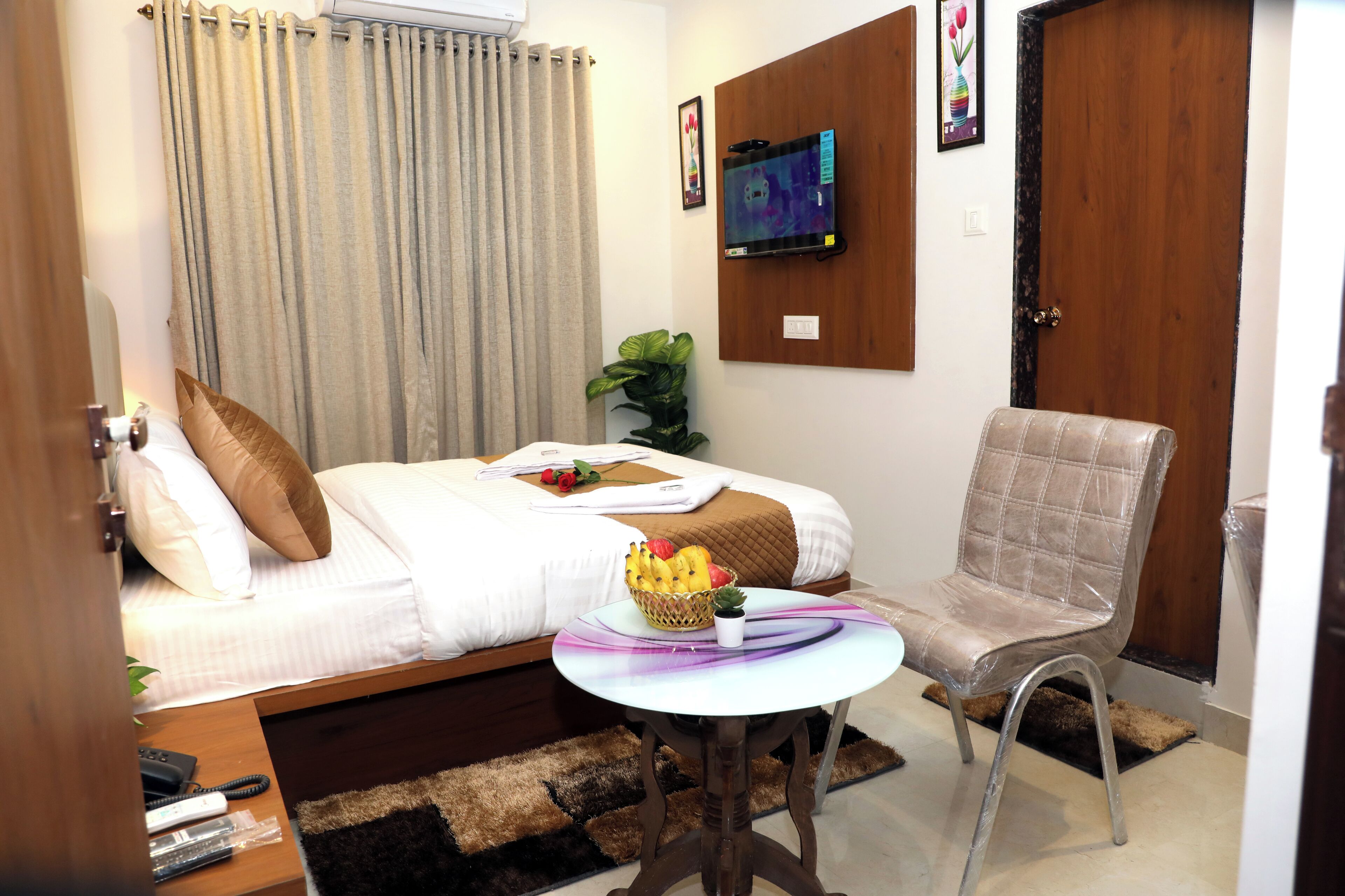 Camera d'albergo con un letto, un tavolino con un cesto di frutta, una sedia e una televisione appesa al muro.