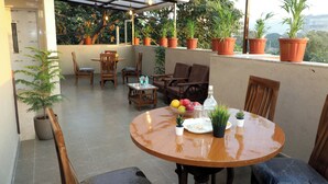 Un área de estar al aire libre con techo, una mesa redonda de madera, sillas y macetas con plantas.