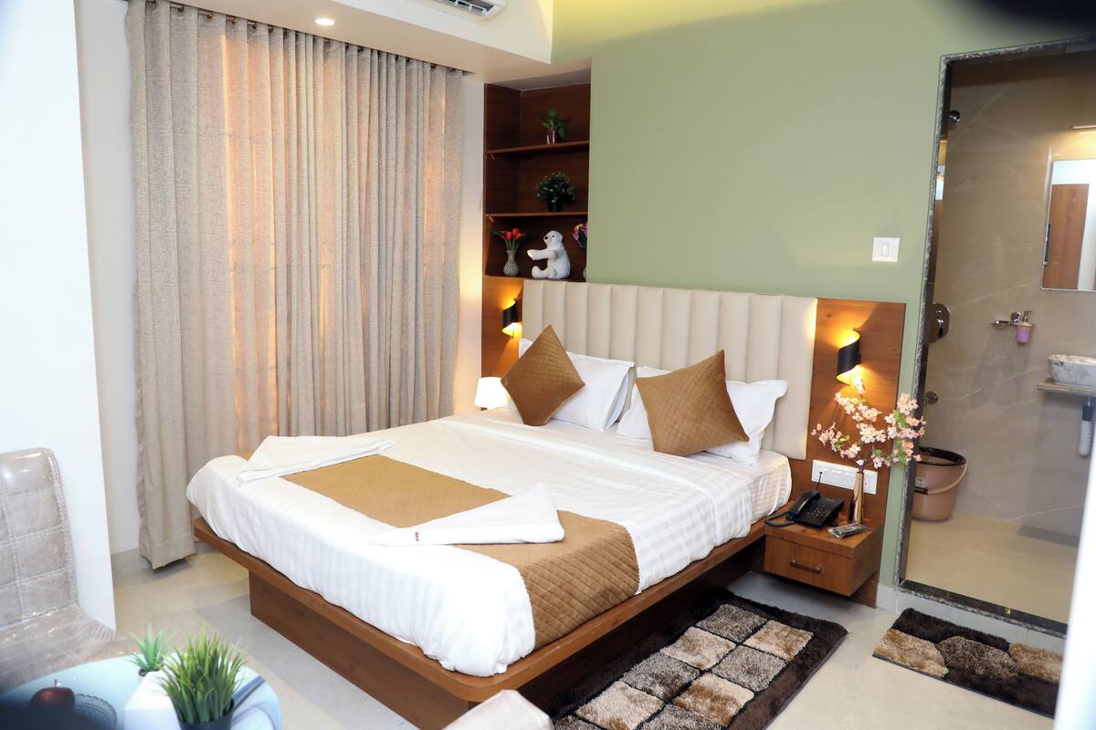 A modern hotel room with a large bed, bedside lamps, a small nightstand, and a bathroom visible through an open door.