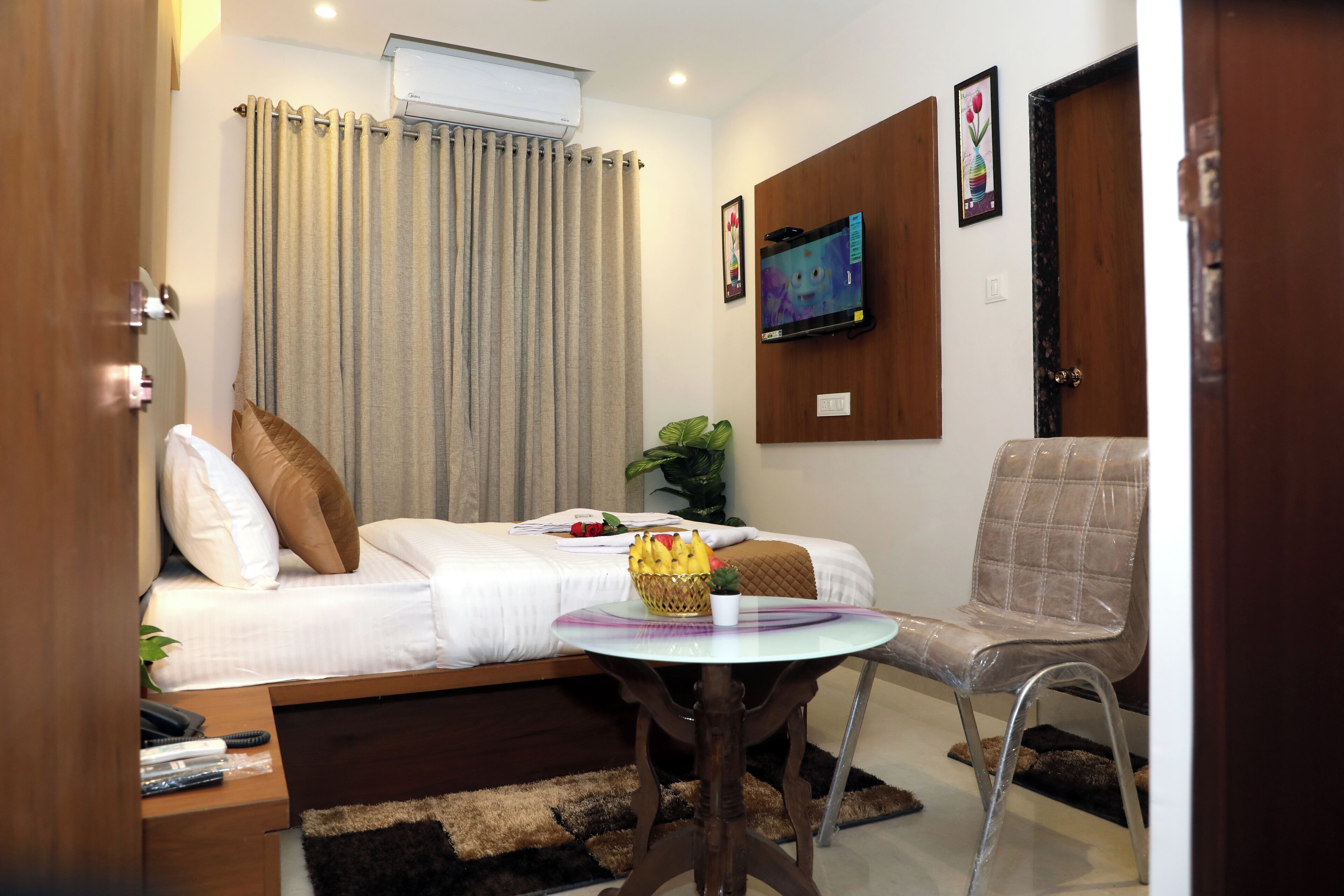 Une chambre d’hôtel avec un lit, une petite table sur laquelle se trouve un panier de fruits, une chaise, un téléviseur fixé au mur et un appareil de climatisation.
