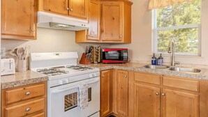 Una cocina con armarios de madera, una estufa blanca, un microondas rojo y una ventana con persianas.