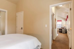 Un dormitorio con una cama, una puerta y un pasillo que conduce a una sala de estar con un sofá y una lámpara.
