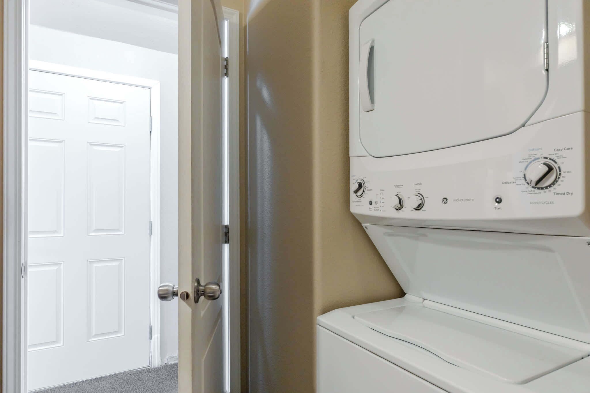 Een wasruimte met een voorlader wasmachine en droger, een deur en een beige muur.