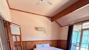 Un dormitori amb llit, ventilador de sostre, aparell d'aire condicionat i finestra amb vista a arbres.