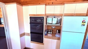 Una cuina compacta amb armaris de fusta, un forn negre, un microones i un frigorífic de tons clars.