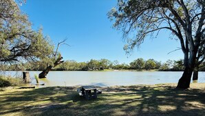 Zona de pícnic a la vora d'un llac, amb taula i bancs, envoltada d'arbres i un cel serè.