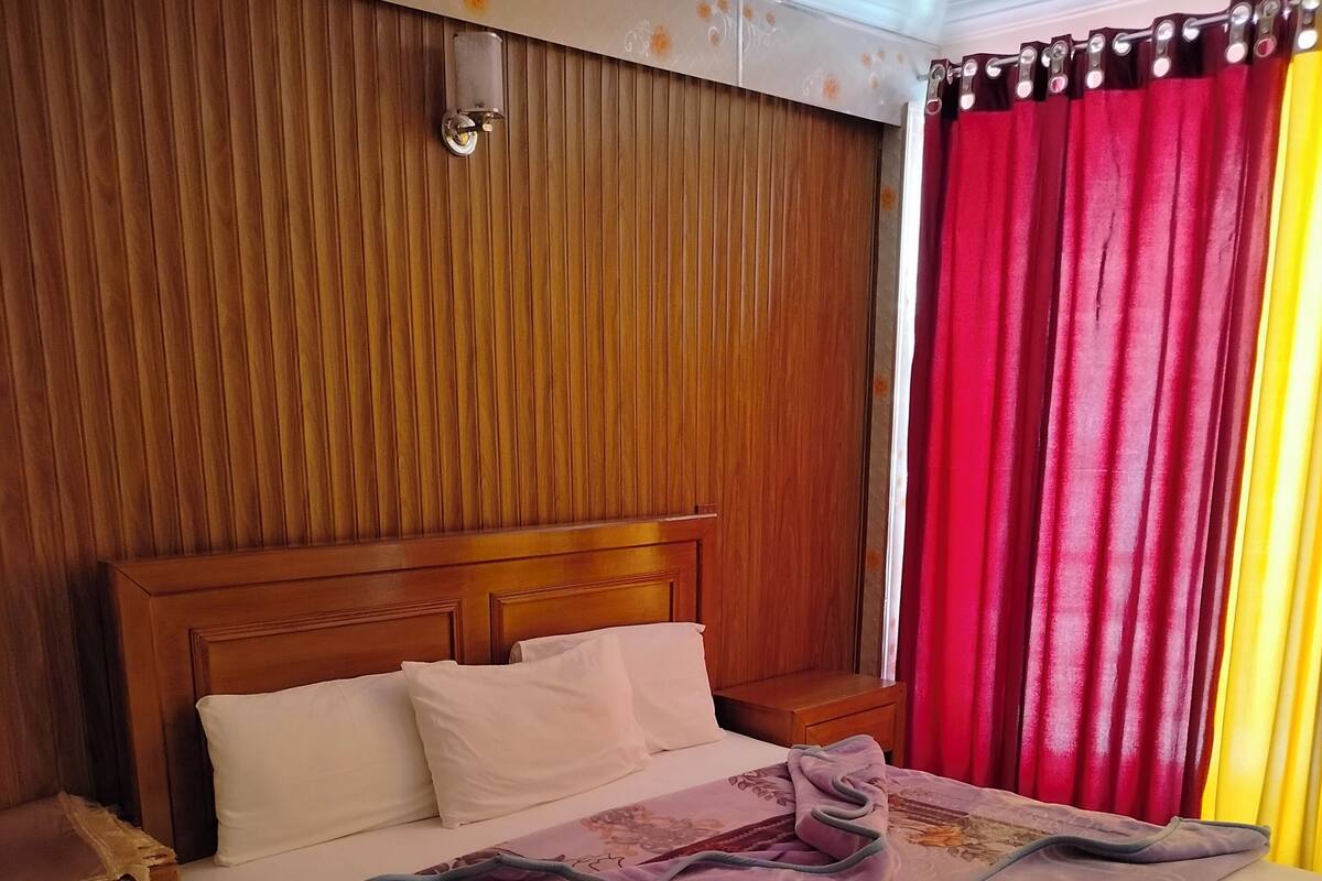 Cama bem arrumada com manta roxa, cabeceira de madeira e almofadas brancas.