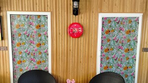 A room with a wooden panel wall, two wicker chairs with red cushions, a small table with pink napkins, and a floral wallpaper. - Hotel Copacabana (Abbottabad)