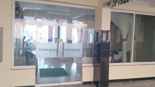 A hotel entrance with a glass door, a sign reading "Copacabana Take a Break," and a view of the interior through the glass. - Hotel Copacabana (Abbottabad)