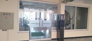 Entrada de un hotel con puerta de cristal, un cartel que dice "Copacabana Take a Break" y vista del interior a través del cristal.